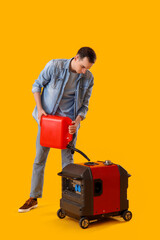 Young man with canister and portable gasoline generator on yellow background