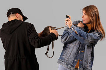 Young woman with pepper spray defending herself against thief on grey background