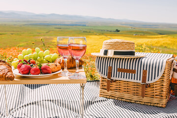 Spring or summer picnic with croissants, fruits and rose wine on the meadow full of wildflowers.