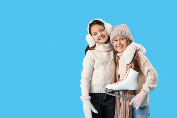 Little girls in winter clothes with ice skates hugging on blue background