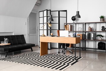 Interior of modern office with workplace, shelving unit and couch