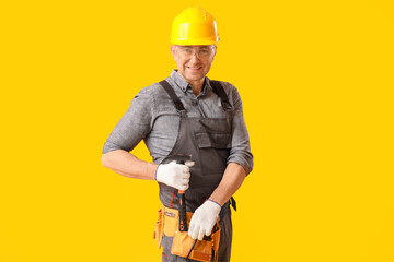 Mature carpenter putting hammer in bag on yellow background