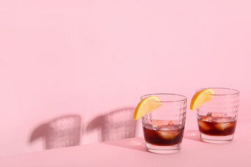 Glasses of rum with ice cubes and lemon slices on pink background