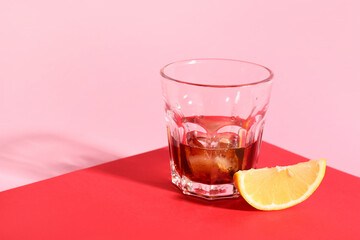 Glass of rum with ice cubes and lemon slice on colorful background