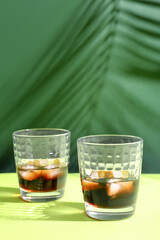 Glasses of rum with ice cubes on green background