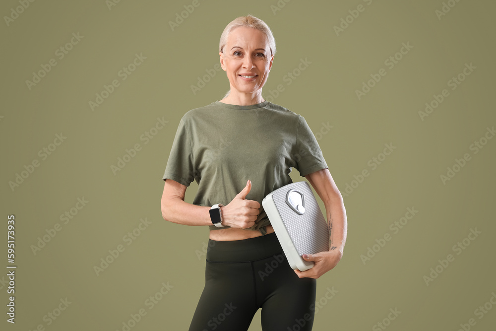 Wall mural Sporty mature woman with scales showing thumb-up on green background