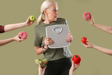 Sporty mature woman holding scales and female hands with food on green background