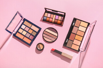 Different palettes of eyeshadows and lipstick on pink background