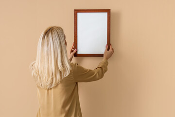 Mature woman hanging blank frame on beige wall, back view