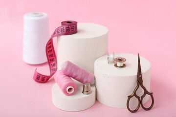 Podiums with tailor's supplies on pink background