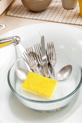 Bowl with cutlery and cleaning sponge in sink, closeup