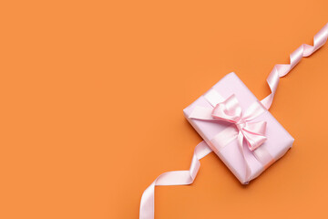 Gift box with beautiful bow and ribbon on orange background