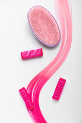 Pink hair strand with curlers and brush on white background