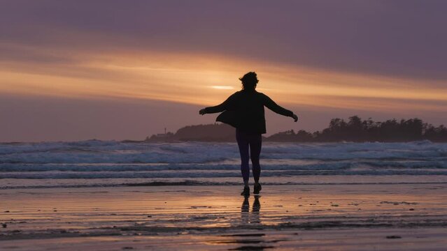 Adventurous Woman Standing on the Sandy Beach on the West Coast of Pacific Ocean. Cox Bay in Tofino, Vancouver Island, BC, Canada. Adventure Travel. Slow Motion