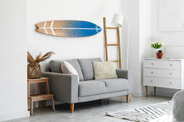 Interior of light bedroom with surfboard, sofa and commode