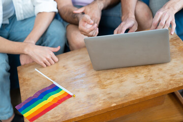 Fototapeta na wymiar Triple young man sitting in the living room while using laptop to video call with rainbow flag on desk. LGBTQ people lifestyle and love emotion. LGBT social network. selective focus
