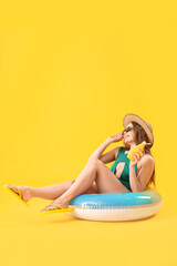 Beautiful young woman with sunscreen cream and inflatable ring on yellow background