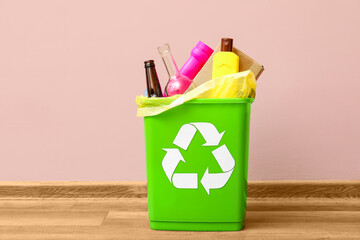 Trash bin with different garbage near pink wall