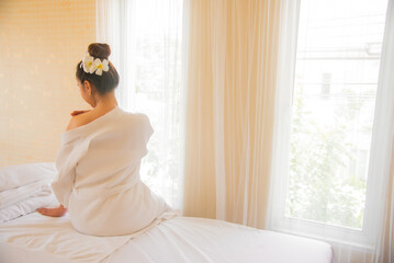 Beautiful woman in a white robe sitting with open shoulders on the bed in the spa room preparing for a massage by professional masseuses with peace of mind.