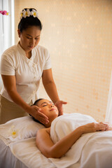 Vertical picture of professional masseuse doing head massage beautiful asian woman with smile on her face in spa room.