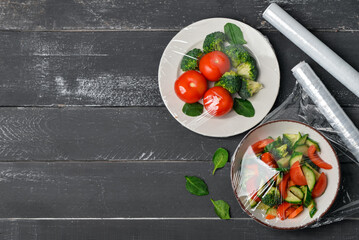 Bowl and plate with salad wrapped with stretch wrap on dark wooden background