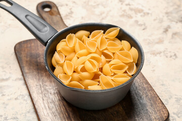 Pot with raw conchiglie pasta on grunge background