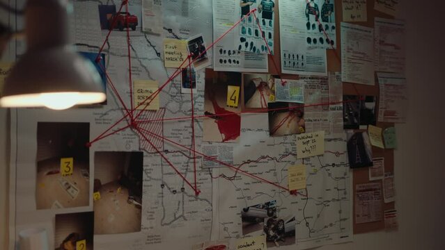 Crime investigation materials connected by red thread on pinboard hanging on the wall at the police station during night. Medium shot, no people