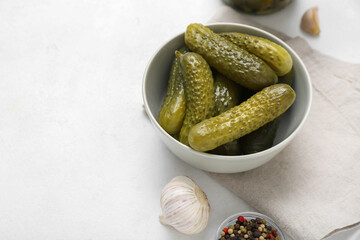 Bowl with tasty fermented cucumbers on light background