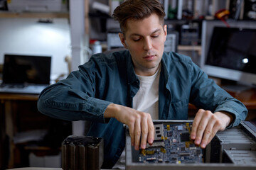 Young caucasian man disassembles broken computer. Computer service and repair concept. Computer disassembling in repair shop, workshop. Electronic development by professional technician