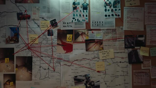 Investigation board with crime scene pictures and reports, mugshots, fingerprints, map, sticky notes and photos of suspects pinned to board and linked by red thread. Close-up view