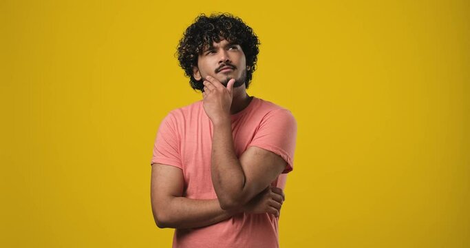 Pleased thinkful indian man is raising-up his finger while coming up with an idea standing isolated over yellow background in studio
