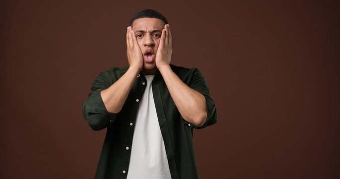  shocked and surprised young african american man puts his hands to his head and face