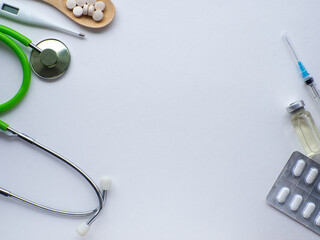 Pills in wooden spoon, thermometer, stethoscope and syringe on white background