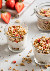 Two granola and yogurt portions with fresh strawberries in light kitchen.