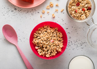 Granola with strawberry and milk in pink bowl plate on light background.