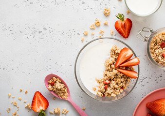 Strawberry organic granola with milk and pink spoon on light kitchen board.