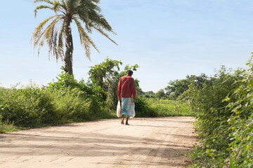 A village man going to shopping to a village market. A lungi wearing man walking with a sack or bag in a sunny day in a rural area of Bangladesh.
