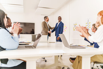 Office Handshake Celebration - Wide shot of a diverse office, two people shaking hands in the...