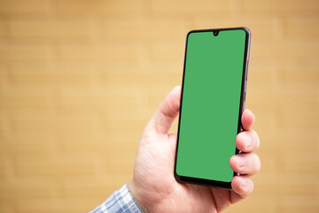 hand holding a smartphone in vertical orientation with green screen over brick background