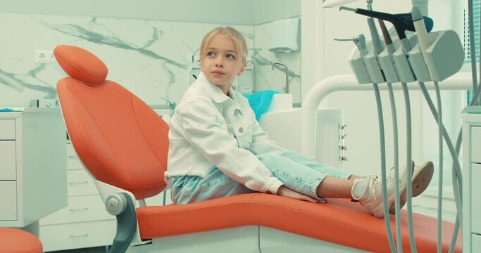 Young fearful little patient scared during a dental check-up at clinic, sitting on chair and waiting for doctor, fear. fobia, slow motion side view treatment, medicine