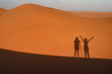 Shadow of a couple on sand dunes at sunset
