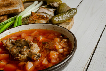 Homemade ukrainian borsch - beetroot soup in a bowl. Green onion, bread, bacon with herbs and pickles 