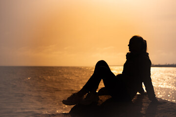 silhouette of a girl sitting on a stone on the sea at sunset, close-up on the silhouette there is a place for an inscription