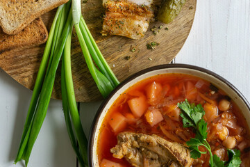 Homemade ukrainian borsch - beetroot soup in a bowl. Green onion, bread, bacon with herbs and pickles 