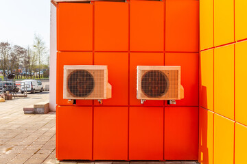 Two air compressors installation on orange wall outside.