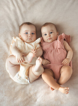 Vetical photo of two sisters baby girls in similar cotton clothes lying on bed. Fraternal twins .