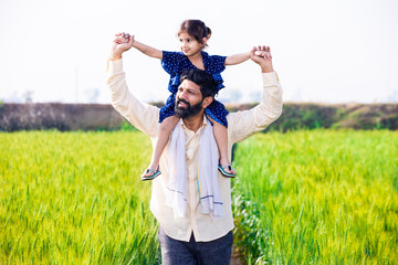 Happy Indian little daughter sitting on father shoulder having fun walking in wheat agriculture...