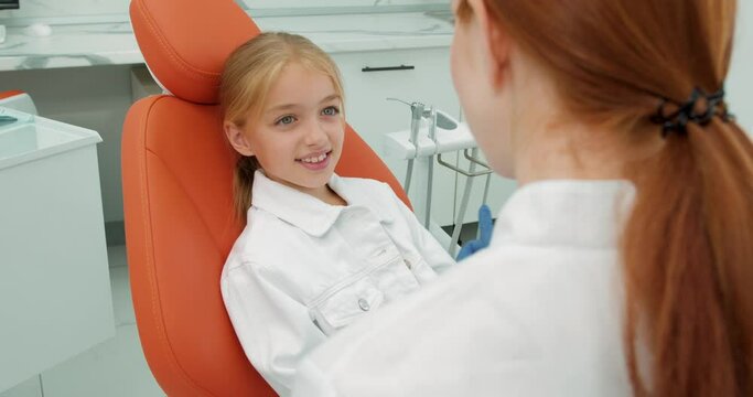 happy brave caucasian child sit on chair in dental clinic with opened mouth while dentist checking teeth, side view, professional stomatologist in white medical uniform before treatment