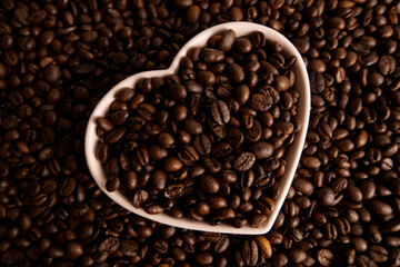 Close-up roasted coffee beans in a heart-shaped plate on a coffee background