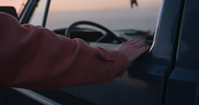 Detail of a young man closing the door to his vintage van to walk into the sunset at the cliffs of the Western Algarve during golden hour, Portugal
